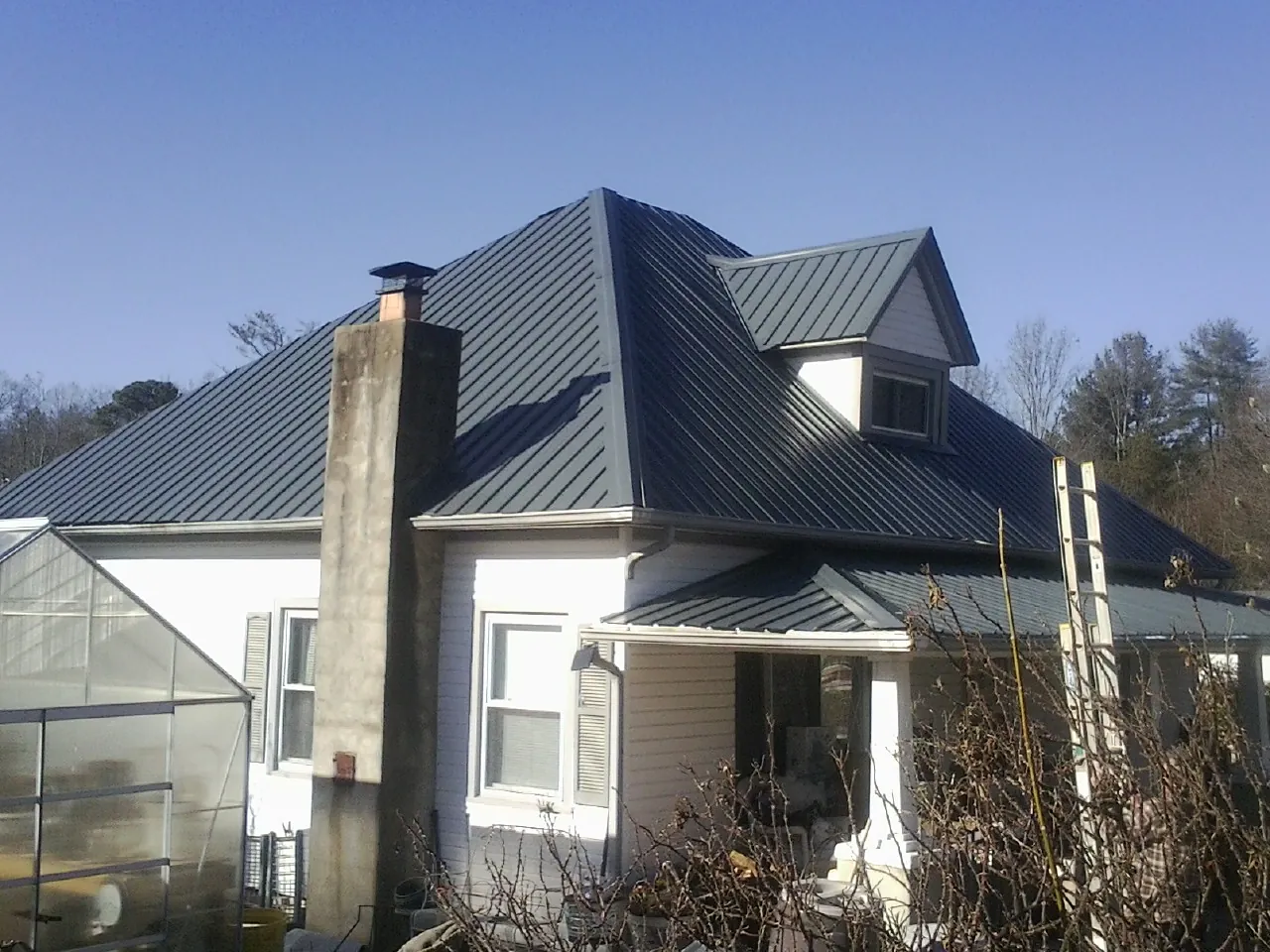 Dark blue standing seam metal roof on a white farmhouse with dormer — Slate & Tile Roof Repair by Roofing Brothers in Mc Bee