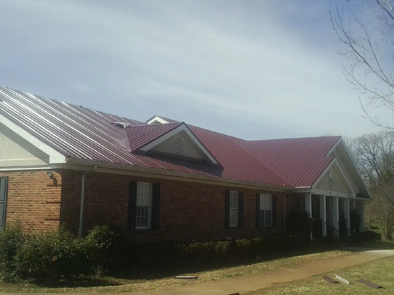 Red metal roof with gabled entries on a long brick building, from a Hail Damage Roof Repair job in Mc Bee