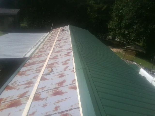 Old rusted panels beside newly installed green metal roofing — Wind Damage Roof Repair by Roofing Brothers in Mc Bee
