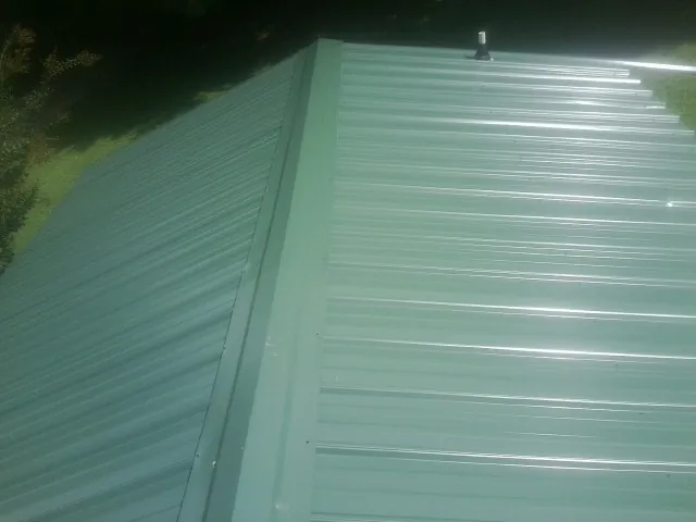 New green metal panels meeting at the ridge of a roof — Flat Roof Repair work by our crew in Mc Bee