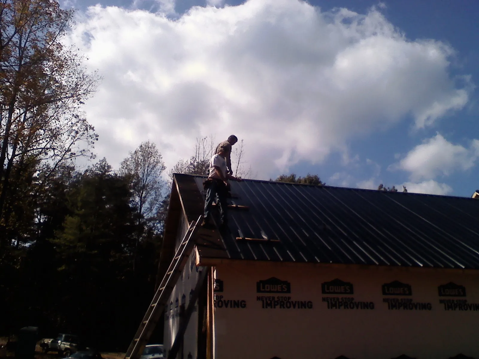 Roofer fastening dark metal panels high against a cloudy sky, from a Roof Inspection job in Mc Bee