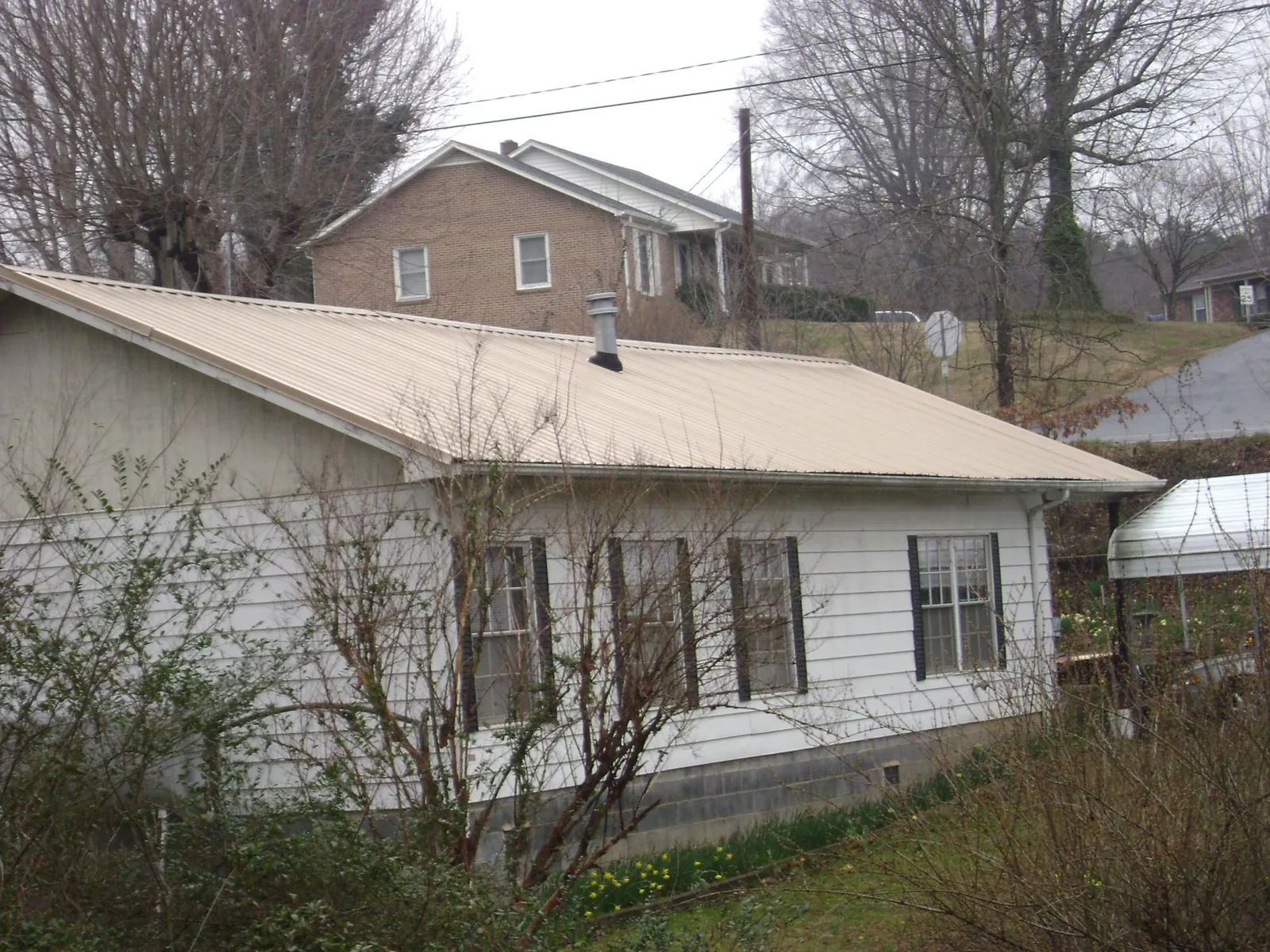 Tan metal roof on a white sided house set into a hillside — Commercial Roofing by Roofing Brothers in Mc Bee