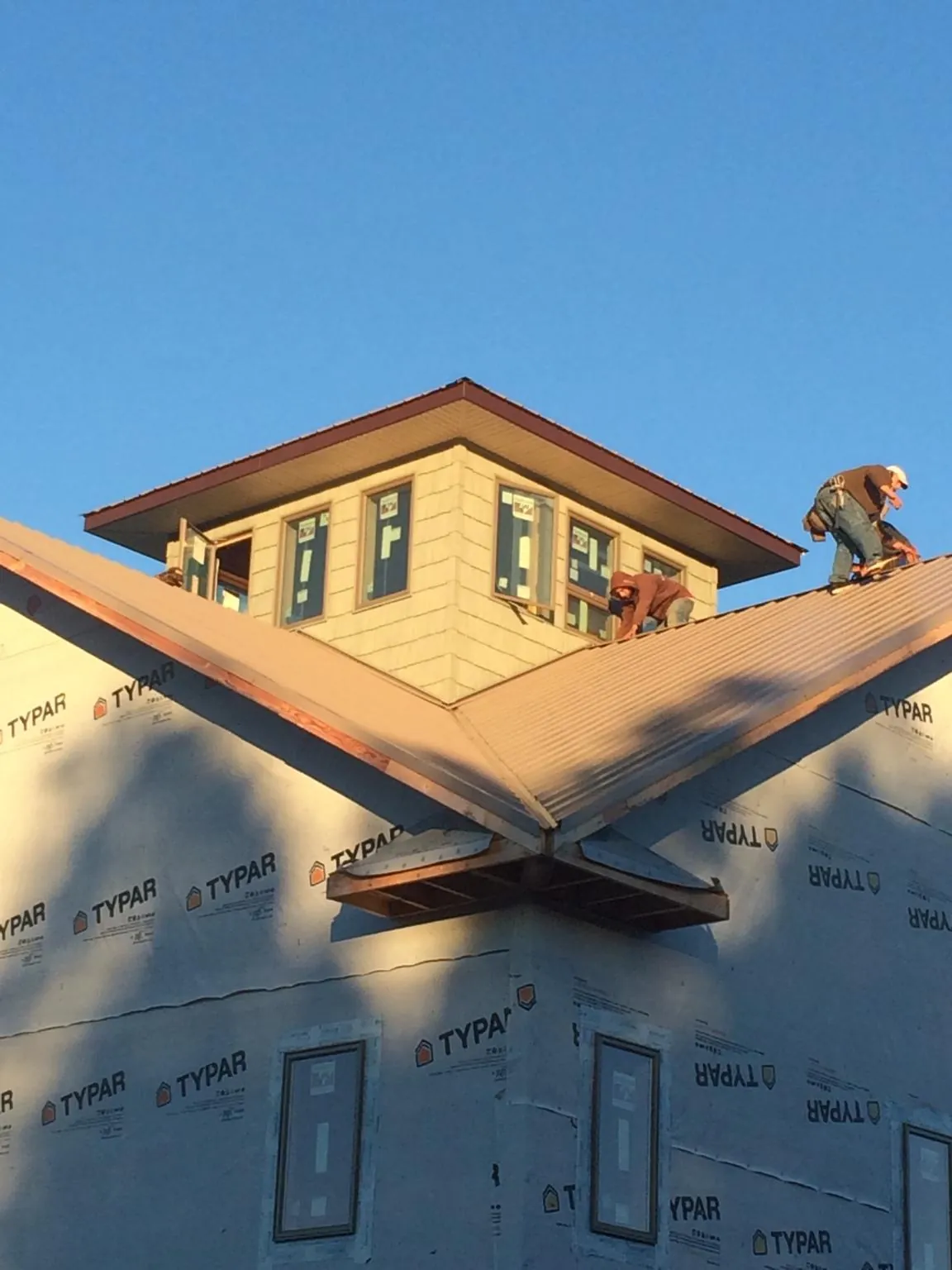 Roofers working around a rooftop cupola on a new metal roof at sunset — Roof Waterproofing in Mc Bee by Roofing Brothers